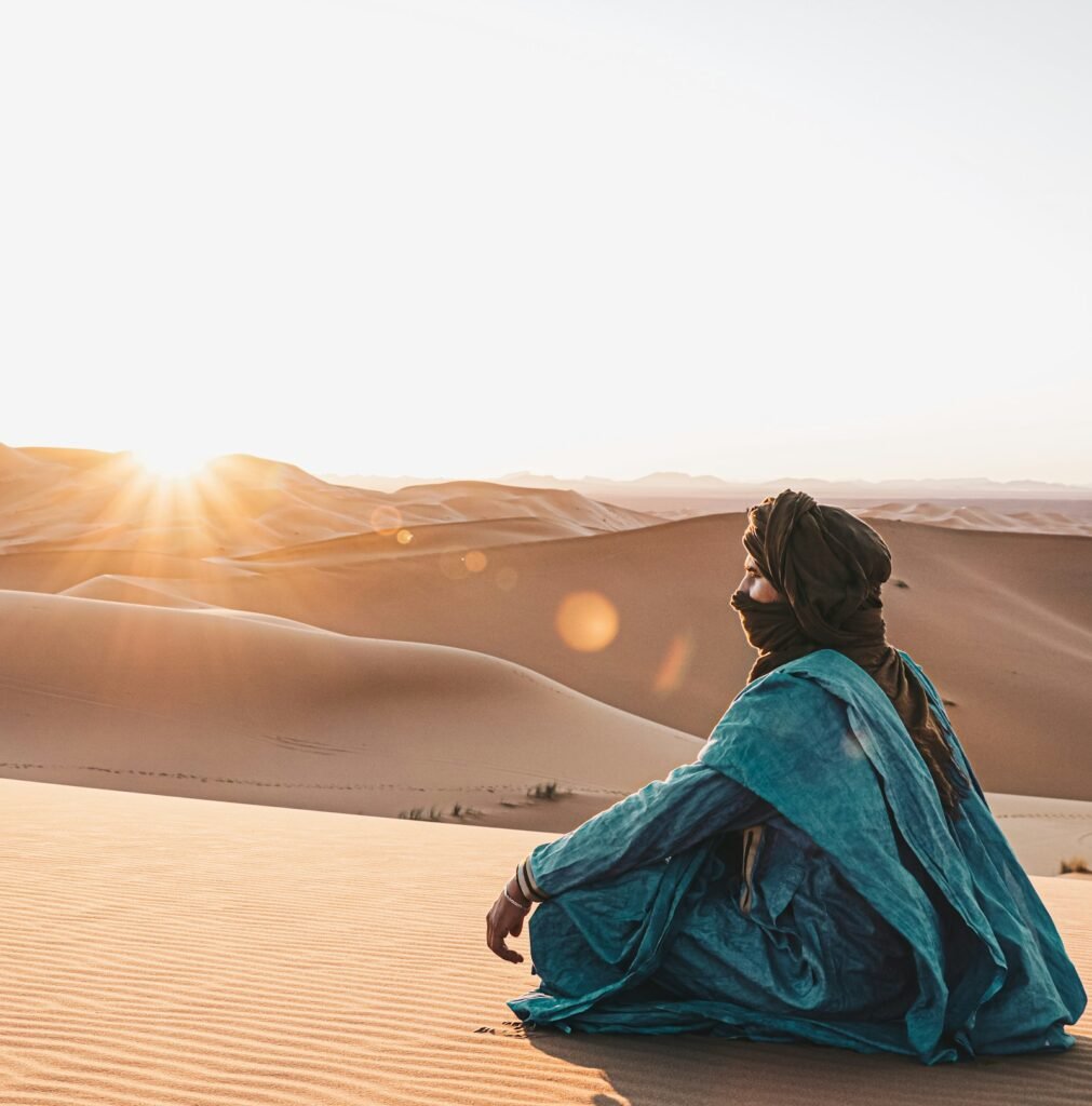 Traveller in a blue scarf watching the sun set over the Sahara dunes
